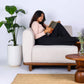 Serene Duo modular modern sofa with integrated wooden side table in neutral fabric and solid teakwood base with a woman sitting on it and reading a book