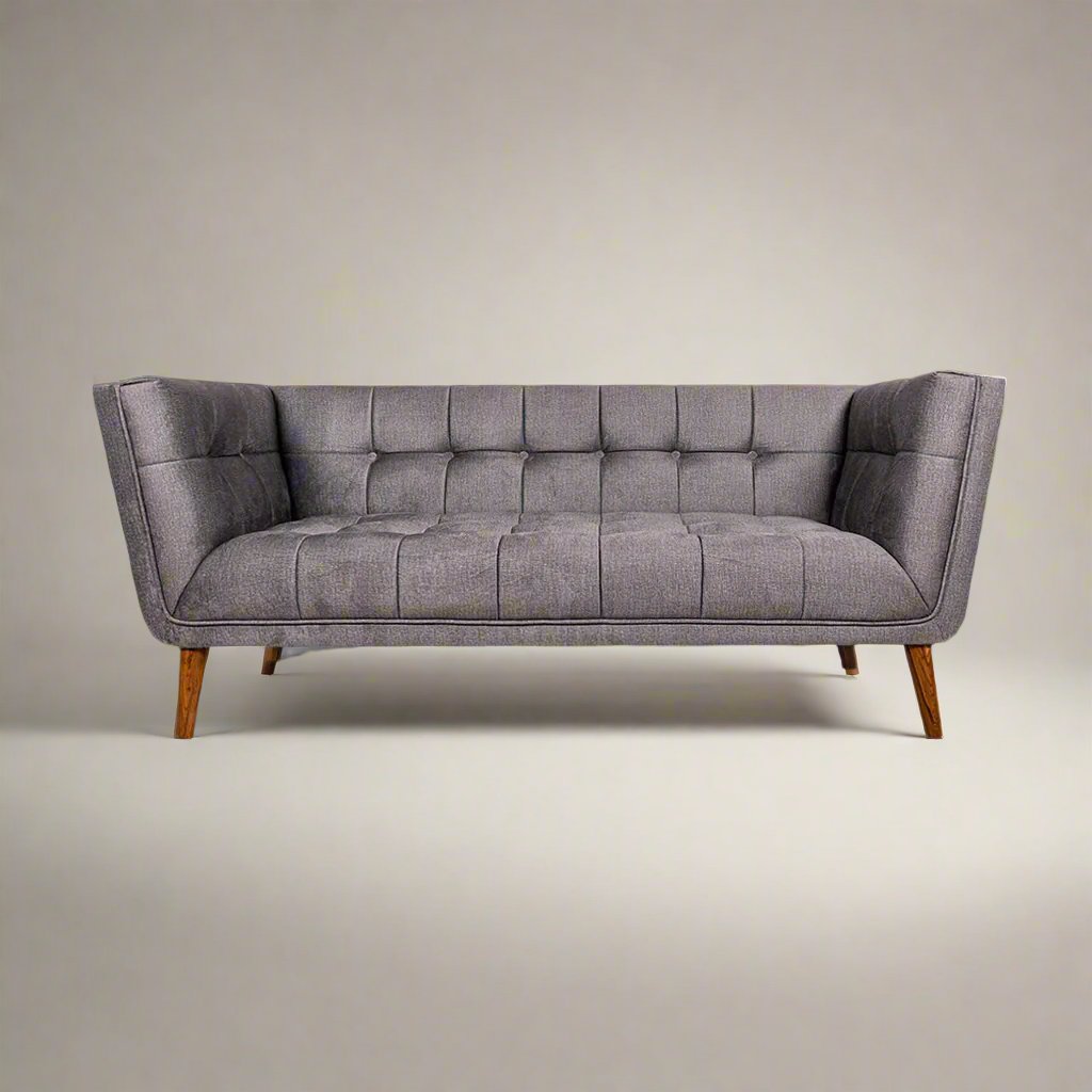 A gray upholstered tufted mid-century modern sofa with wooden legs, featuring a broad profile, deep button tufting, and flared armrests.