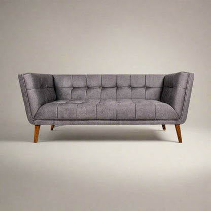 A gray upholstered tufted mid-century modern sofa with wooden legs, featuring a broad profile, deep button tufting, and flared armrests.